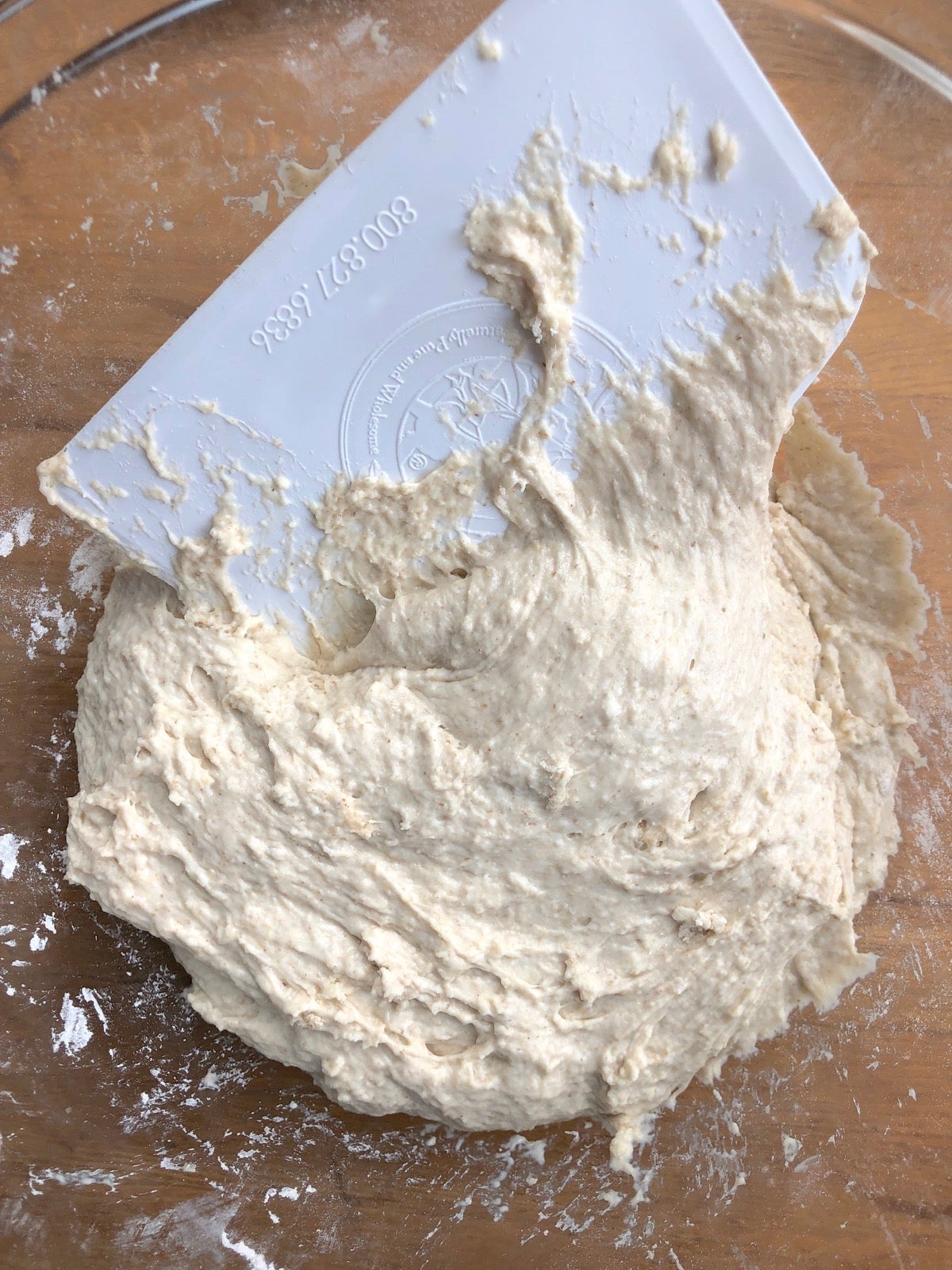 Using a bowl scraper to stir together sourdough bread ingredients in a bowl.